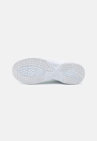 Semelle de chaussure de sport blanche avec une texture en motif de grille sur un fond gris clair, vue du dessous.