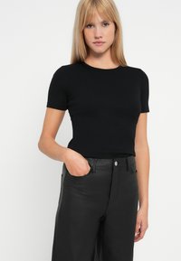Tricou scurt cu mânecă, negru, cu un design ajustat, decolteu rotund și textură netedă, asortat cu pantaloni strânși, negri, cu talie înaltă, lucioși.