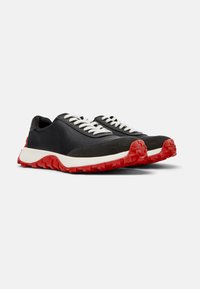 Scarpe in pelle nera con lacci bianchi, caratterizzate da una tomaia testurizzata, suola in gomma rossa con scanalature profonde per la presa e un design della punta arrotondata.