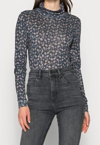 Långärmad polokrage i genomskinlig marinblått tyg med ett paisleymönster i pastellfärger, kombinerad med högmidjade svarta jeans.