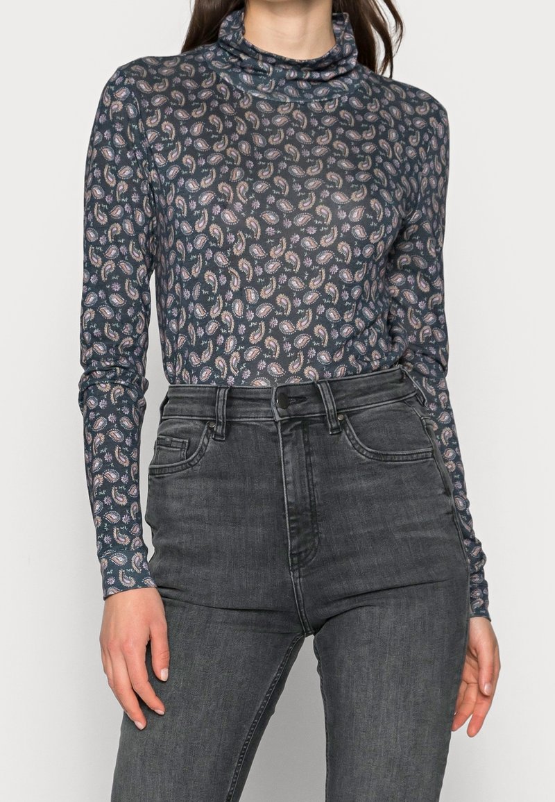 Långärmad polokrage i genomskinlig marinblått tyg med ett paisleymönster i pastellfärger, kombinerad med högmidjade svarta jeans.