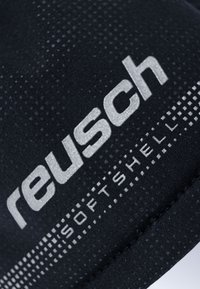 Schwarzer Softshell-Stoff mit glatter Textur, ausgestattet mit dem silbernen "Reusch"-Logo und gepunkteten Mustern am Rand.