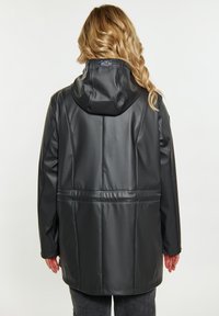 Svart vattentät parkas med huva, med en slät, glänsande textur, sömnadsdetaljer och en baketikett nära halsringningen.