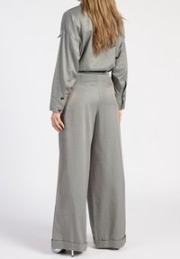 Světle šedý, volný dvoudílný outfit s dlouhým rukávem na knoflíky a kalhotami širokého střihu. Hladká textura, minimální design a ohrnuté manžety.