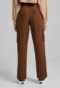 Bruna cargobyxor med sidofickor, hög midja, rak ben och en mjuk textur, kombinerat med vita sneakers.