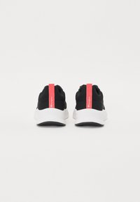 Scarpe sportive nere con tomaia in maglia, suola bianca e un prominente linguetta rossa con dettagli del logo. Design minimalista con materiale testurizzato.