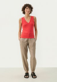 Rød ribbet ærmeløs top med V-hals, parret med lysebeige bukser med elastiske manchetter og sorte strappy sandaler. Glat stofstruktur.