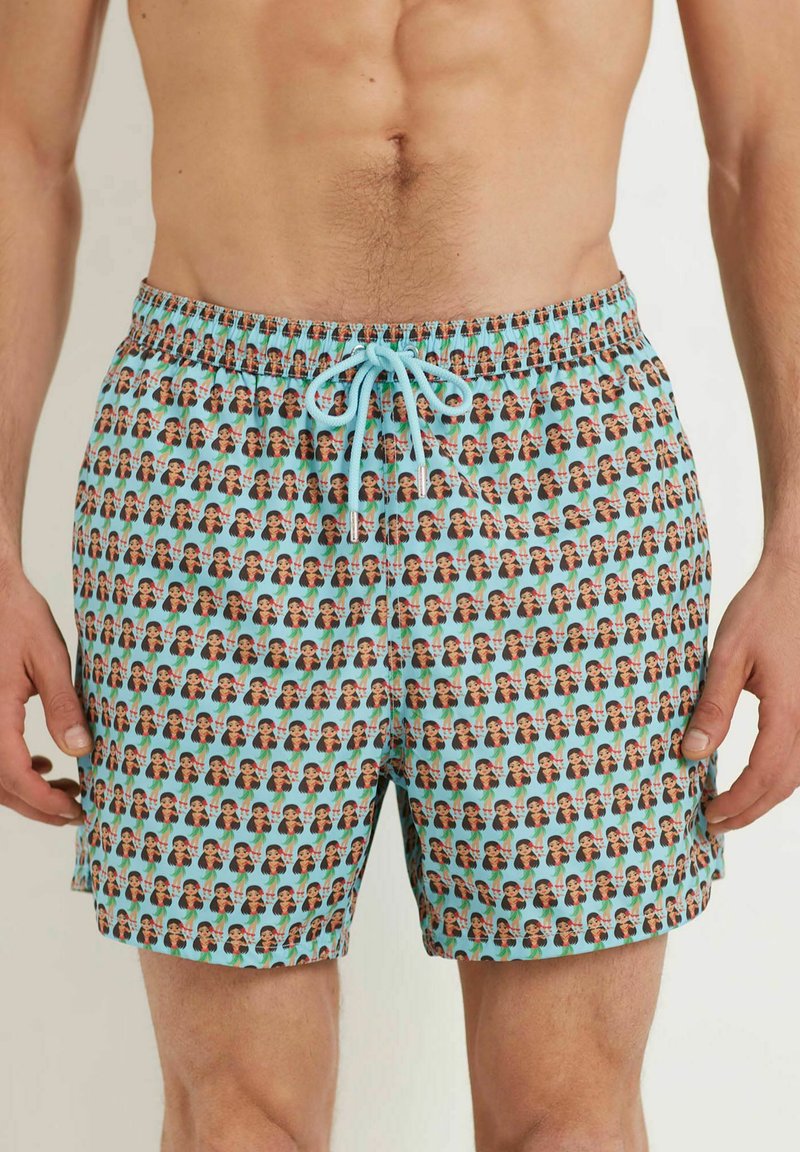 Maillots de bain avec une base turquoise, présentant un motif répétitif de visages. Ceinture élastique avec cordon de serrage pour un ajustement réglable.