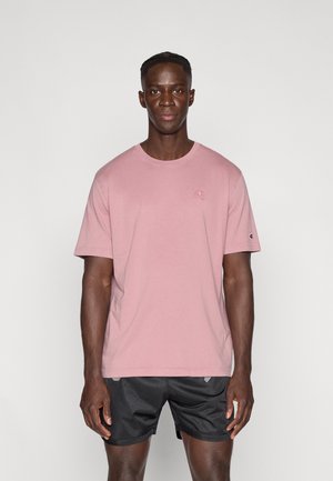 Vaaleanpunainen puuvillainen t-paita, jossa on lyhyet hihat ja pyöreä pääntie. Edessä pieni logo ja hihojen logokoriste.