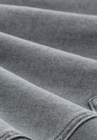Gros plan d'un tissu en denim gris plié montrant la texture et les détails des coutures.