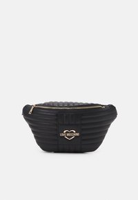 Černá prošívaná taška z umělé kůže s zakřiveným tvarem, zlatým zipem a vyraženým logem ve tvaru srdce uprostřed. Hladká textura.