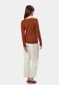 Maglione marrone lavorato a maglia con maniche lunghe e orlo a costine, abbinato a pantaloni bianchi a gamba larga e mules con tacco marroni. Design semplice, senza motivi.