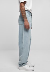 Light blue denim jeans with a loose fit, straight legs, and visible stitching. Paired with white sneakers, showcasing a casual look.