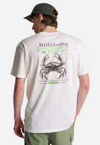 Λευκό βαμβακερό t-shirt με γραφικό μαύρου καβουριού και κείμενο σε μωβ και πράσινο στην πλάτη. Στρογγυλή λαιμόκοψη και κοντά μανίκια.