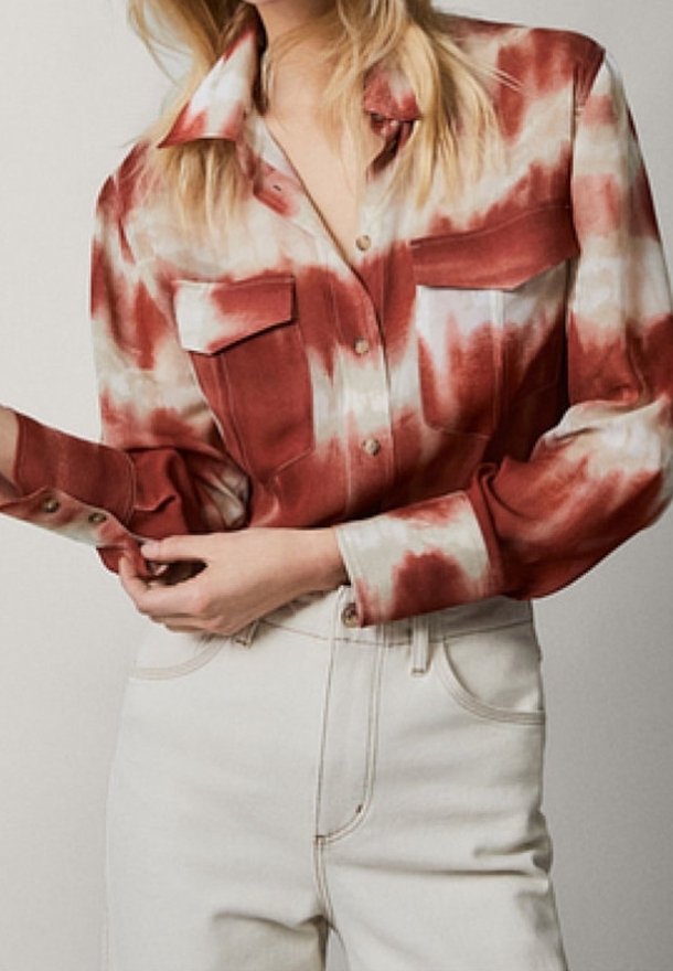 Chemise boutonnée rouge et blanche en tie-dye avec deux poches poitrine, manches longues et col pointu, associée à un jean blanc taille haute.