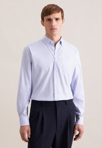Camicia azzurro chiaro con bottoni e una piccola texture a motivo, con una tasca sul petto, abbinata a pantaloni blu scuro.