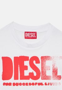 Λευκό βαμβακερό μπλουζάκι με υπερμέγεθη κόκκινα γράμματα "DIESEL" με υφή και το σλόγκαν "FOR SUCCESSFUL LIVING" σε μικρότερο κείμενο από κάτω.