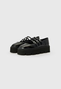 Black patent leather platform shoes with thick, textured soles, featuring three crossed straps and silver accents.