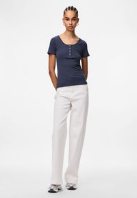 Ναυτικό ριγέ κοντομάνικο μπλουζάκι με στρογγυλή λαιμόκοψη και πεντάκτινο κουμπί, συνδυασμένο με πλατιά παντελόνια σε κρεμ απόχρωση και ασημί αθλητικά παπούτσια.