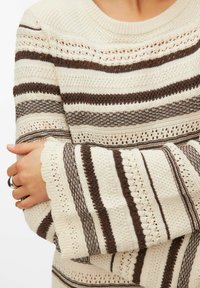 Stickad tröja med växelvis ljusgräddvita och bruna ränder, detaljerad med hålmönster och vågiga muddar för textur och design.