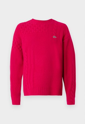 Suéter de punto fucsia con diferentes patrones de trenzas, cuello redondo y puños de canalé. Pequeño logo de la marca en la parte delantera.