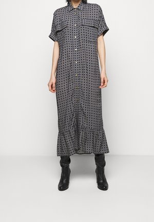 Femme portant une robe midi à manches courtes, boutonnée, à motifs avec des poches avant, associée à des bottes noires à talons sur un fond uni.