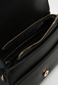 Borsa a tracolla in pelle nera con più scomparti, texture liscia, zip e dettagli hardware color oro. L'interno è rivestito in tessuto.