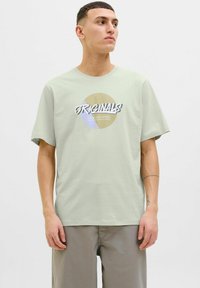Lys grøn bomulds t-shirt med grafisk tryk, der har teksten "ORIGINALS" og cirkulære farve accenter. Rund hals og korte ærmer.