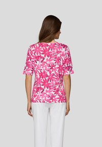 Short-sleeve shirt in pink and white floral pattern. Cotton blend fabric with a relaxed fit and round neckline. White pants complement the look.