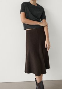 Harmaa lyhythihainen villapaita, joka on yhdistetty ruskeaan villasta valmistettuun A-linjaisiin hameeseen. Hameessa on sivusauma ja hillitty rakenne. Ruskeat nilkkurit.