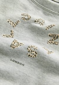Ljusgrå sweatshirt med leopardmönstrade bokstäver som stavar "LONDON", med en ribbad rundhalsning. Mjuk textur med en avslappnad design.