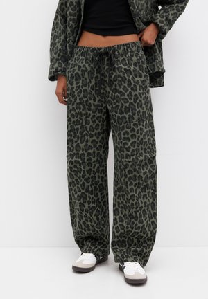 Green and black leopard print loose pants with elastic waistband and black drawstring, worn with white sneakers and matching jacket.