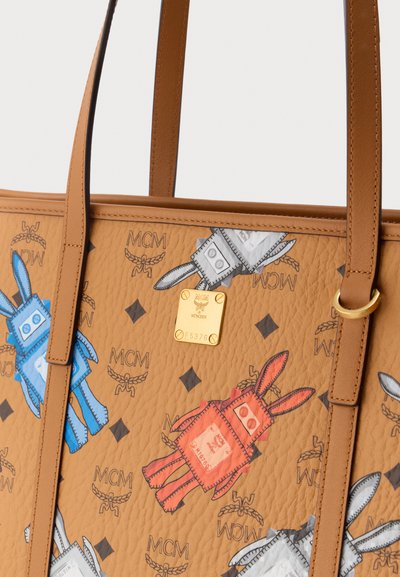 Τσάντα χειρός MCM από ταμπά δέρμα με εκτυπώσεις ρομποτικού κουνελιού σε μπλε, κόκκινο και γκρι, και χρυσή πλακέτα με το λογότυπο, με λαβές και ραφές από ταμπά δέρμα.