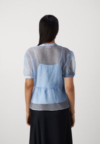 Light blue sheer blouse with short puff sleeves, textured fabric, and a peplum waist. Features a back cutout and collar.