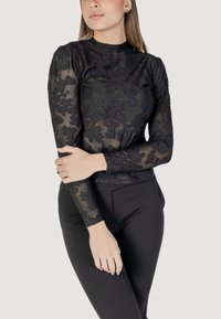 Top in pizzo nero con un alto collo e maniche lunghe. Tessuto trasparente con motivi floreali, abbinato a pantaloni neri a vita alta.