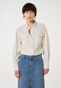 Helles rosa Hemd mit Knöpfen und zwei Brusttaschen, kombiniert mit einem Jeansrock mit einem vorderen Schlitz und Druckknopfdetails.