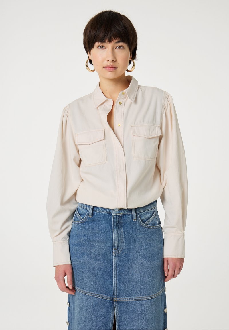 Helles rosa Hemd mit Knöpfen und zwei Brusttaschen, kombiniert mit einem Jeansrock mit einem vorderen Schlitz und Druckknopfdetails.