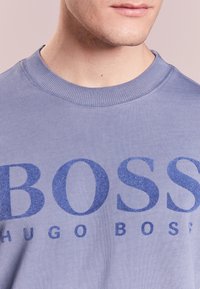 Light blue sweatshirt made of cotton with a round neckline. Features a bold blue "BOSS" logo and smaller "HUGO BOSS" text below.