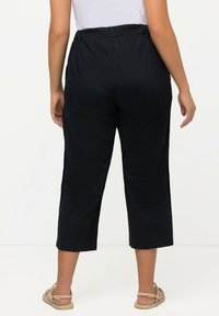 Svarta cropped byxor med elastisk midja, med sidoflikar och en mjuk textur, stylade med platta sandaler.