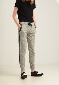 Grå sweatpants med sidelommer og sorte accentstriber, parret med en tekstureret sort kortærmet top og sorte og hvide sko.