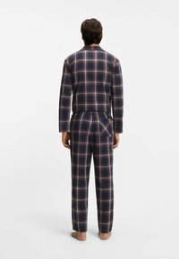 Mörkblå pyjamaset i rutigt mönster med långärmad tröja och löst sittande byxor, med klassiskt rutmönster i röda och vita accenter, tillverkat i bomullstyg.