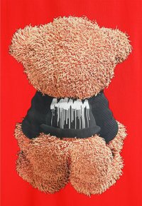 Camiseta roja con un gráfico de oso de peluche texturizado, con una superficie marrón clara y una camiseta negra que representa goteos blancos.