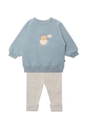 Blaue Sweatshirt mit rundem Ausschnitt, mit einem lächelnden Toast im Becher-Design. Graue Leggings mit Muster und umgeschlagenen Säumen.