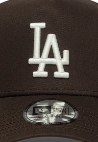 Braune Baseballmütze mit weißem, gesticktem "LA" auf der Vorderseite. Verstellbarer Riemen auf der Rückseite, mit einem silbernen New Era-Logopatch darunter.