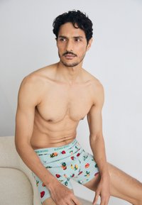 Männerboxershorts aus lichtblauem Stoff mit einem Blumenmuster. Elastischer Bund mit dem Aufdruck "BJÖRN BORG." Das Modell sitzt poses und ist oberkörperfrei.