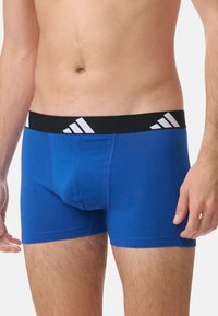 Boxers en coton bleus avec une taille noire ornée de rayures diagonales blanches et une coupe ajustée. Le tissu semble lisse et extensible.