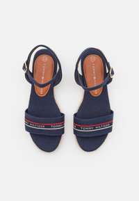 Navyblauwe espadrille sandalen met een denim bovenwerk, gekenmerkt door een brede band met rood en wit Tommy Hilfiger-logo, en een bruine binnenzool.