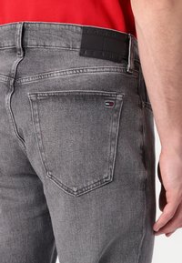 Los jeans de mezclilla grises presentan un diseño estándar de cinco bolsillos con una etiqueta en la cintura negra en relieve con logotipos y un pequeño emblema tricolor en el bolsillo trasero.