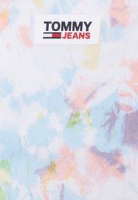 Etiqueta Tommy Jeans em tecido de tie-dye pastela, apresentando espirais de rosa, azul, amarelo e verde, com uma textura suave e aparência leve.