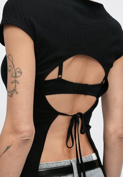 Μαύρο ριμπ τοπ με σχεδιασμό ανοιχτής πλάτης, ρυθμιζόμενους δεσίμους και κούμπωμα με γάντζο. Κοντά μανίκια και υφασμάτινη υφή.